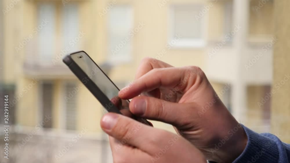 Man holds black smartphone sliding viewing gallery pictures closeup at home by window Man holds black smartphone sliding viewing gallery pictures closeup at home by window