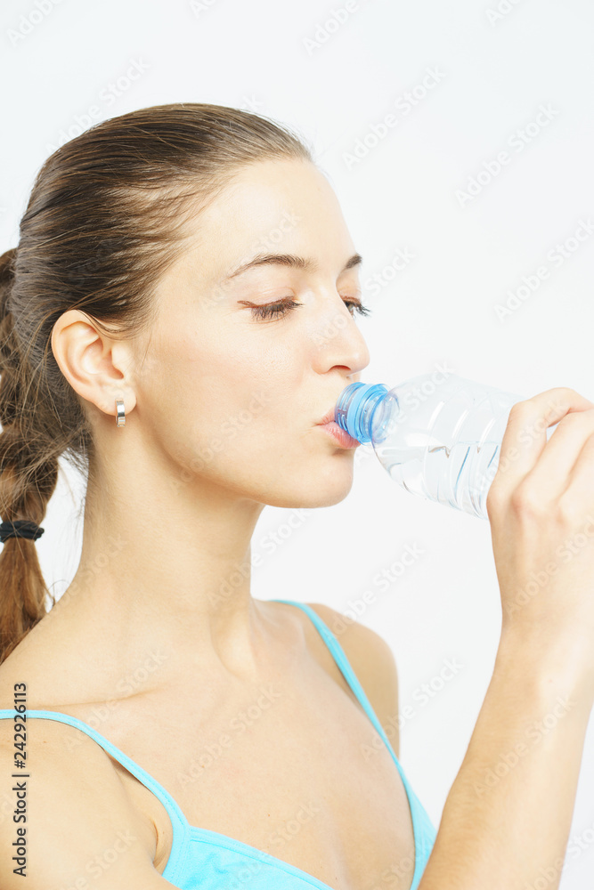 Attractive slim girl in sportswear with a smile opens a plastic bottle with clean water during a workout on a white background. Attractive slim girl in sportswear with a smile opens a plastic bottle with clean water during a workout on a white background.