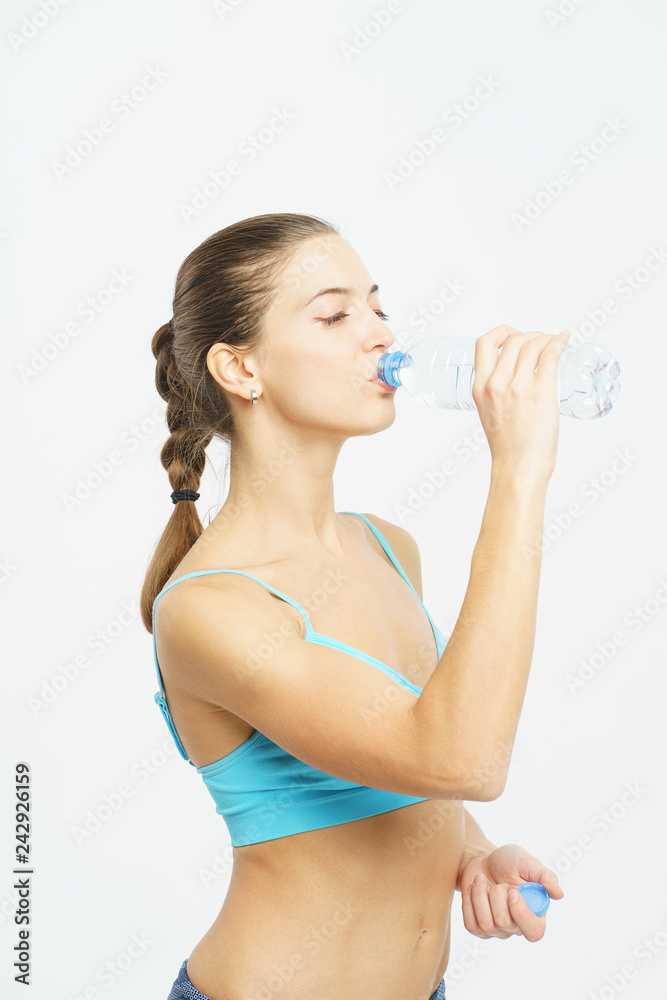 Attractive slim girl in sportswear with a smile opens a plastic bottle with clean water during a workout on a white background. Attractive slim girl in sportswear with a smile opens a plastic bottle with clean water during a workout on a white background.