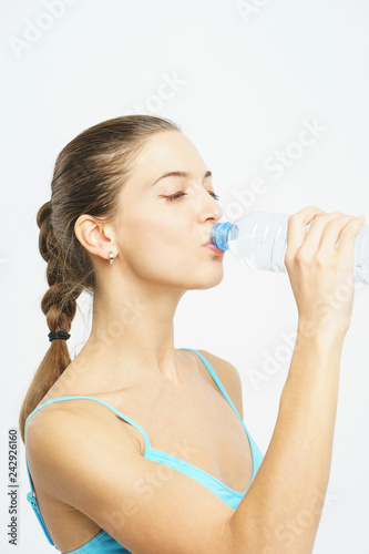 Attractive slim girl in sportswear with a smile opens a plastic bottle with clean water during a workout on a white background. 