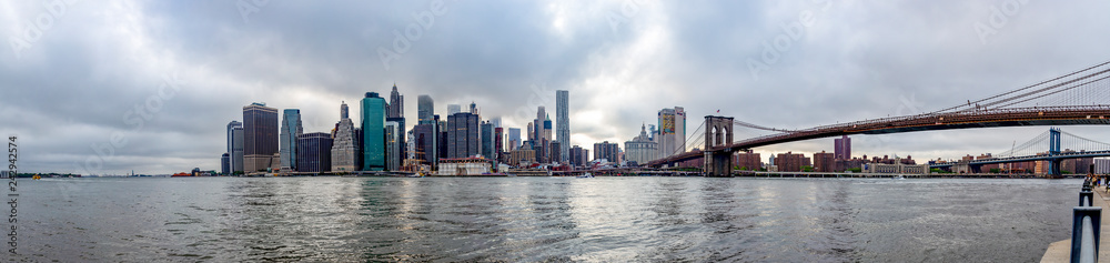 Panorama photo of the Brooklyn Bridge and Manhattan with the tops of the skyscrapers reaching the clouds in New York, United States
