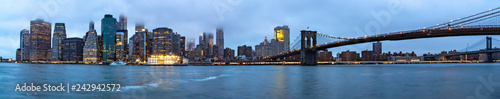 Panorama photo of Manhattan with the tops of the skyscrapers in the clouds and the Brooklyn Bridge after sunset in New York  United States