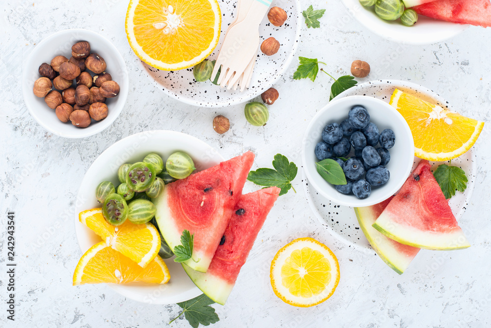 Ingredients of healthy nutrition. Slices of watermelon, blueberries, orange, gooseberries, green berries, nuts, fruit plate. On a light background. Top view. Ingredients of healthy nutrition. Slices of watermelon, blueberries, orange, gooseberries, green berries, nuts, fruit plate. On a light background. Top view.