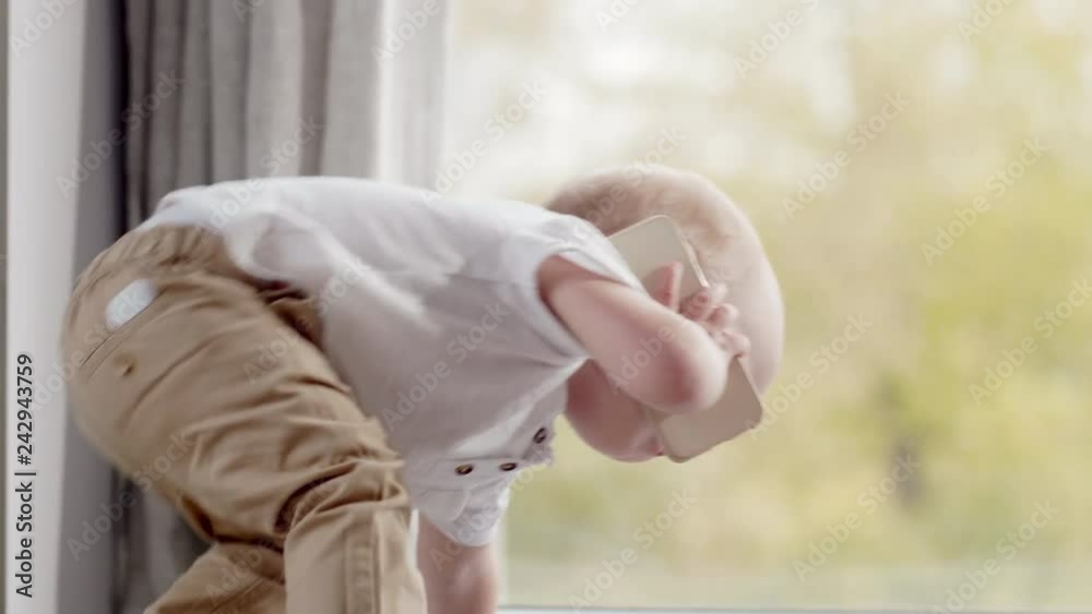 Tilt up of adorable baby boy standing up on bed at home and calling on mobile phone Tilt up of adorable baby boy standing up on bed at home and calling on mobile phone