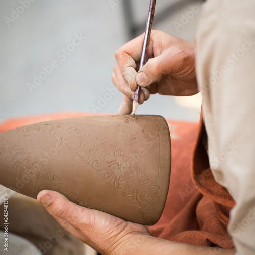 Ceramic workshop, the master puts otnament on unfired earthenware jug. Close-up of master hands. Made by hand, a hobby. Background illustrating the manual work with clay. photo