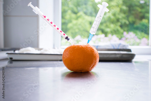 Syringe sticked into orange on wooden table,GMO