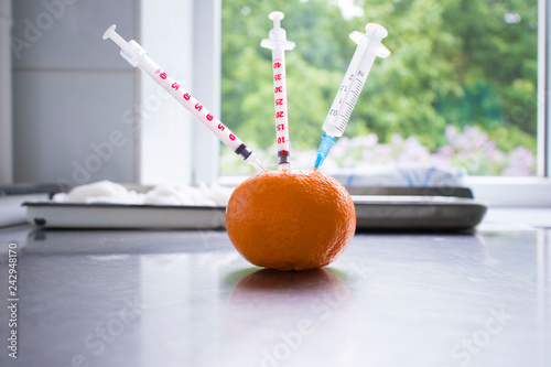 Syringe sticked into orange on wooden table,GMO