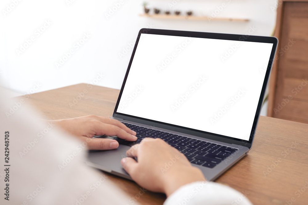 Mockup image of hands using and typing on laptop with blank white desktop screen on wooden table in office Mockup image of hands using and typing on laptop with blank white desktop screen on wooden table in office