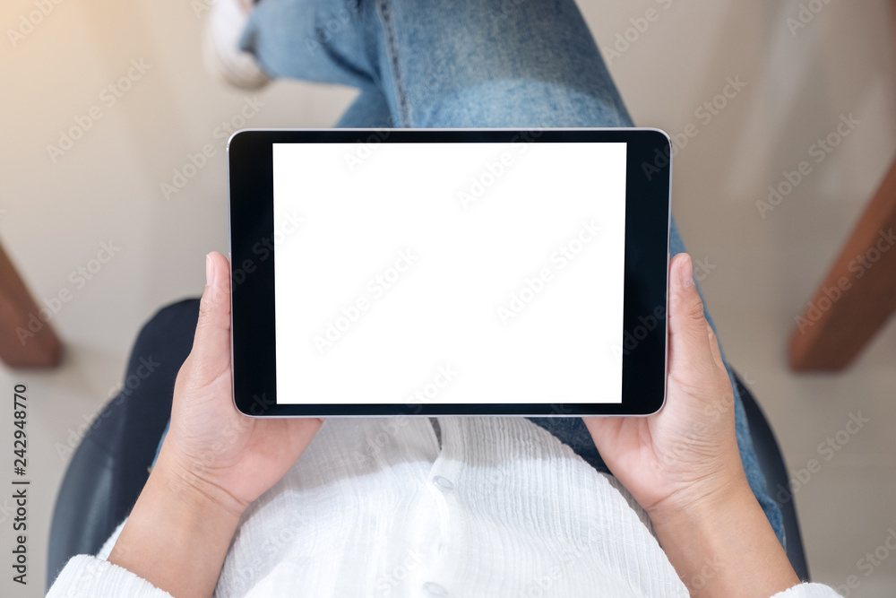 Top view mockup image of a woman holding black tablet pc with blank white screen horizontally while sitting on a chair