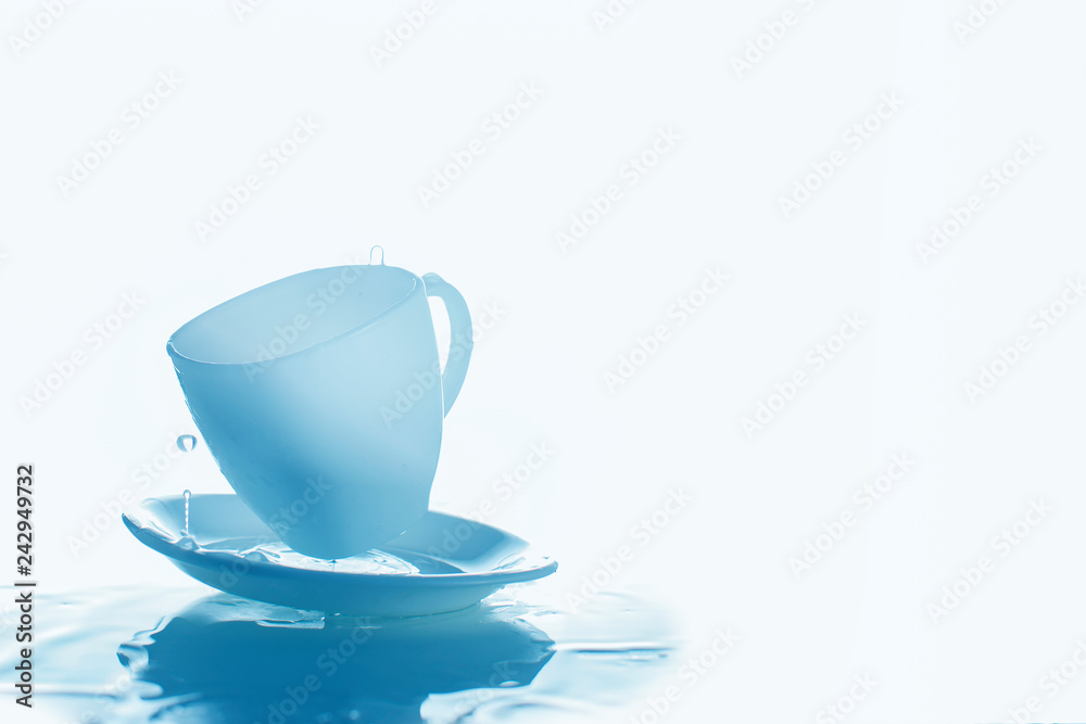 Blue cup and saucer with splashes of water.Glasses and water on a blue background Blue cup and saucer with splashes of water.Glasses and water on a blue background