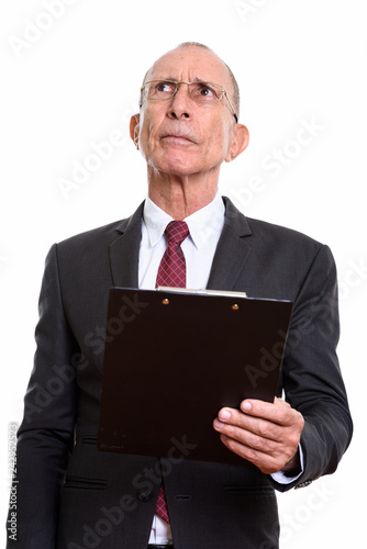 Studio shot of senior businessman holding clipboard while thinki photo