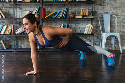 Young fitness woman doing push ups workout on one arm on floor at home