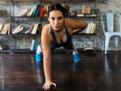 Young fitness woman doing push ups exercise on one hand on floor
