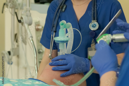 Anesthesiologist makes a general anesthesia to a patient before the surgery pushing a mask to his face with assistant prepares an intubation instrument in foreground close-up photo