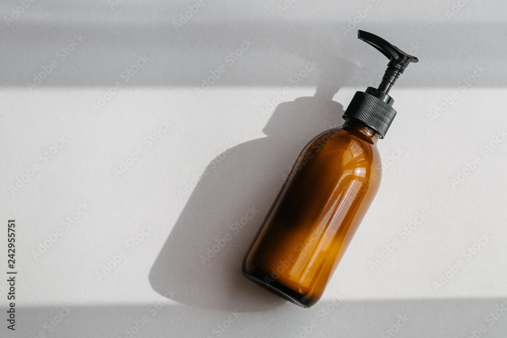 One pump dispenser glass brown bottle for cosmetics, overhead. Direct light. Beauty blogging, salon treatment, minimalism concept One pump dispenser glass brown bottle for cosmetics, overhead. Direct light. Beauty blogging, salon treatment, minimalism concept