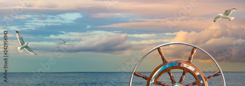 Marine sunrise with cloudy sky in pastel colors and flying seagulls over the ocean. Calm seascape with a skippers wheel on a ship for your concept of sea voyage or nautical expedition. photo