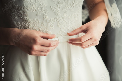 a stylish wedding dress with a white aunt Aivari, in front of a direct light source with elegant details and hands of the bride girl. Copy Space