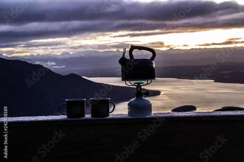 Outdoor cooking equipment or coffee making concept. Scenic landscape view of small mugs and kettle/pot standing on gas stove. Beautiful morning scene up in the Fiordland National Park, New Zealand