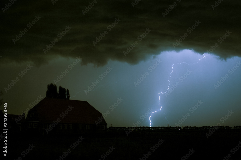 Lightning strike on a dark blue sky over a house silhouette. Photographed when a severe thunderstorm moved over the southwestern part of The Netherlands, September 15th 2016.