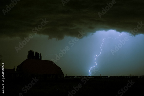 Lightning strike on a dark blue sky over a house silhouette. Photographed when a severe thunderstorm moved over the southwestern part of The Netherlands, September 15th 2016.
