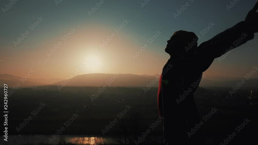 Silhouette of man raises hands up standing back on mountain on the sunset. Freedom concept Silhouette of man raises hands up standing back on mountain on the sunset. Freedom concept