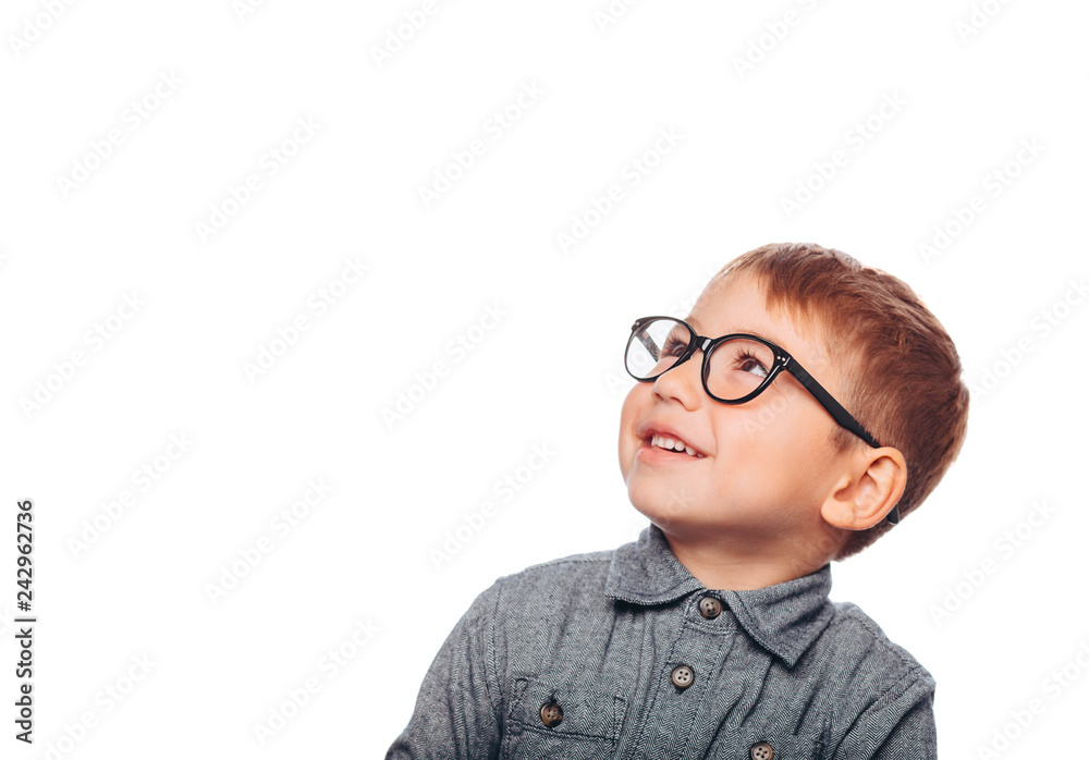 Portrait of little positive boy with eyeglasses smiling at camera looking away, against white background