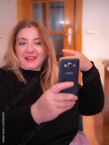 Attractive mature woman takes a selfie with his mobile phone sitting on a sofa