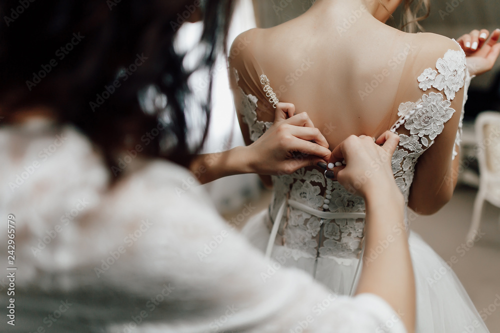 bridesmaid fastens buttons on the wedding dress of the bride