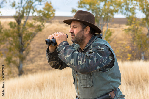 A hunter in a hat with binoculars looks out for prey 