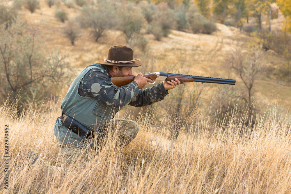 Fototapeta premium Hunter with a hat and a gun in search of prey in the steppe 
