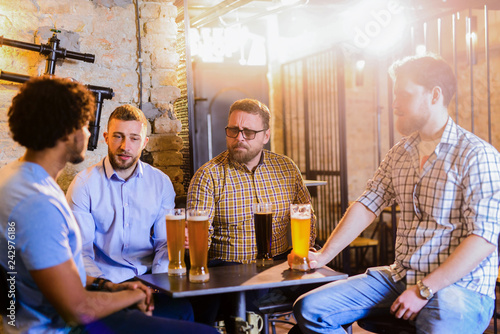Group of man sitting in a bar with glasses full of beer in front of them. Sitting and having fun.