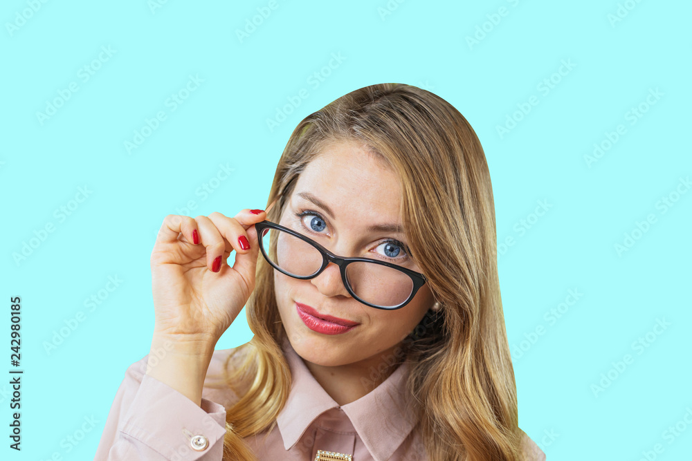 Portrait of a young attractive blonde with glasses that holds glasses with one hand, lower them from the eyes and look into the camera on an isolated background, positive emotions Portrait of a young attractive blonde with glasses that holds glasses with one hand, lower them from the eyes and look into the camera on an isolated background, positive emotions