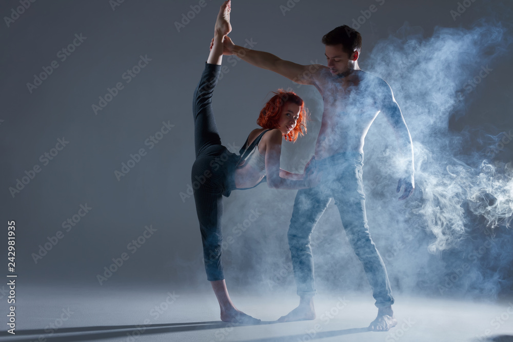 Hip Hop Dancer Nude Girl - Foto Stock Couple in love dancers making dance element in smoke fume on  isolated grey background scene. Redhead woman female dancer athlete gymnast  in overalls with muscle male man in jeans and