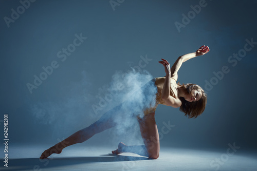 Dancing in cloud concept. Muscle brunette beauty female girl adult woman dancer athlete in fog smoke fume wearing dance bodysuit making emotional dance element performance on isolated grey background