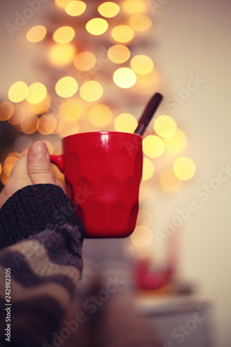 woman's hand with mug of hot drinc against blurred christmas tree background/christmas concept