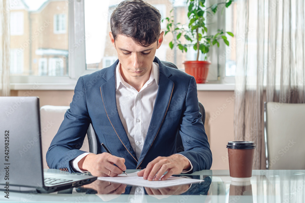 Businessman sitting at the table signing documents in the office. Concept of transactions and work with securities Businessman sitting at the table signing documents in the office. Concept of transactions and work with securities