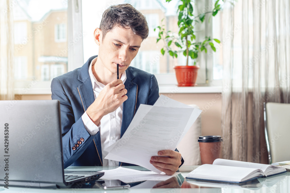 Businessman sitting at a work place examing documents. Concept of the office working with documents Businessman sitting at a work place examing documents. Concept of the office working with documents