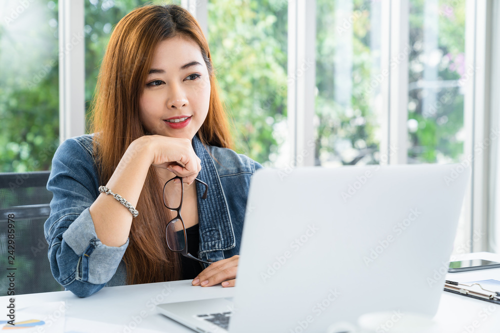 Young asian casual businesswoman sitting smiling working on laptop in modern hom office