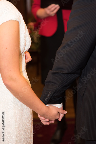 Back view of bride in white dress and groom in suit holding each others hands