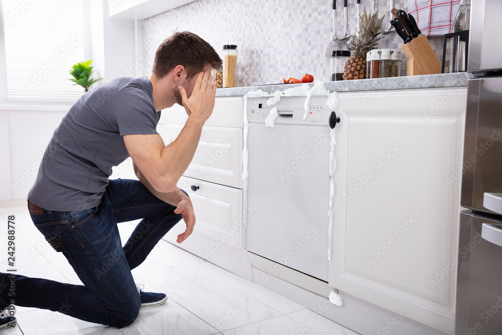 Upset Man Sitting In Front Of Damaged Dishwasher Upset Man Sitting In Front Of Damaged Dishwasher