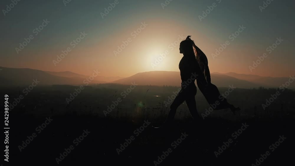 Silhouette of a beautiful young woman running in the mountains with a pareo in her hands. Slow motion. The concept of freedom, ease, success, rest. Sunset