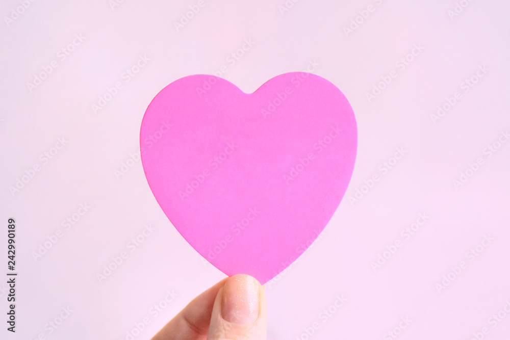 Violet paper heart in white woman hand with blurred pink background with empty space for image or text. Colorful design heart for valentines day. Violet paper heart in white woman hand with blurred pink background with empty space for image or text. Colorful design heart for valentines day.