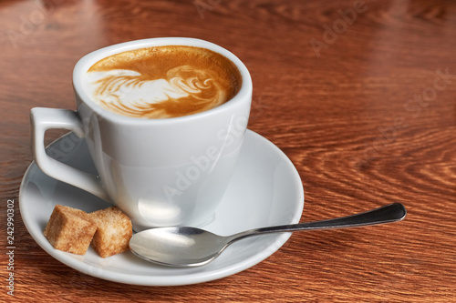 coffee with a pattern of foam is in the saucer, which is a teaspoon and two pieces of cane sugar