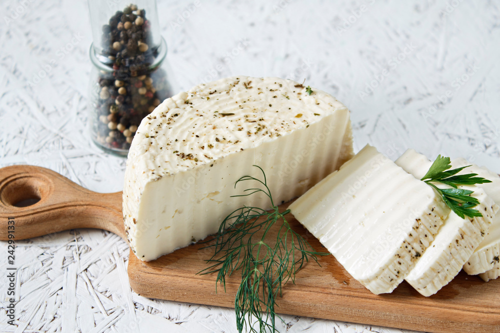 White cheese and spices on a wooden board on a white background White cheese and spices on a wooden board on a white background