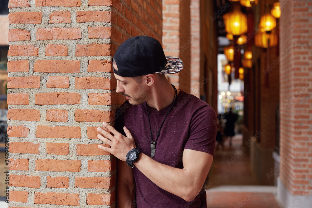 Glad handsome creative young male designer wears fashionable clothes, looks with smile aside, tries to get interesting idea for new project, leans with shoulder on brick wall,being inspired by texture Glad handsome creative young male designer wears fashionable clothes, looks with smile aside, tries to get interesting idea for new project, leans with shoulder on brick wall,being inspired by texture
