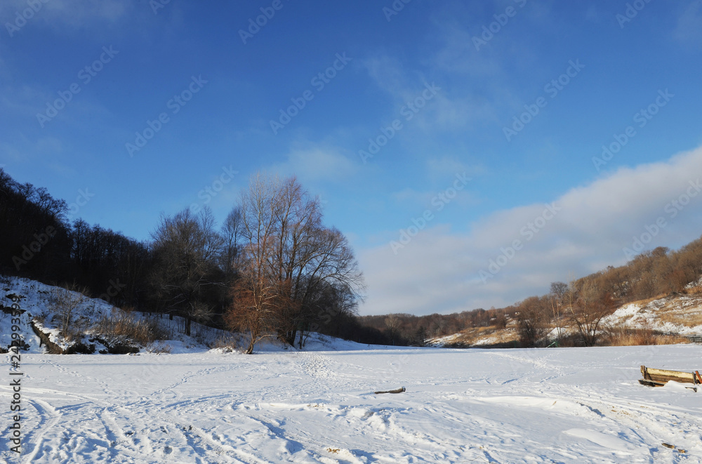 Winter snowy coastal landscape on a sunny day. Frozen river. Clear sky. Open space. Two boats on the shore Winter snowy coastal landscape on a sunny day. Frozen river. Clear sky. Open space. Two boats on the shore