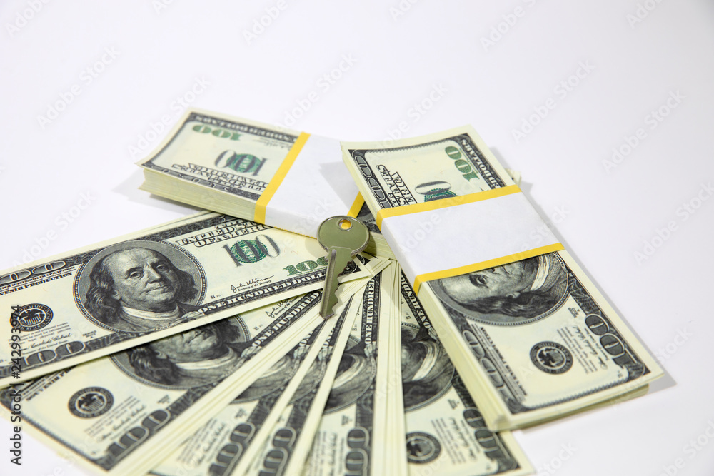 Bundles of hundred dollar banknotes on a white background. House keys. The keys to the apartment on the dollars. Bundles of hundred dollar banknotes on a white background. House keys. The keys to the apartment on the dollars.