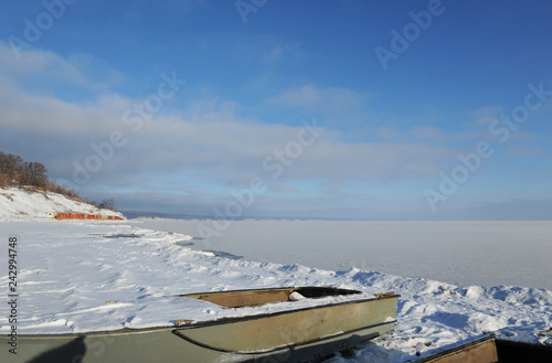 Two abandoned boats on the snowy coast. Winter coastal landscape on a sunny day. Frozen river. Clear sky. Open space.