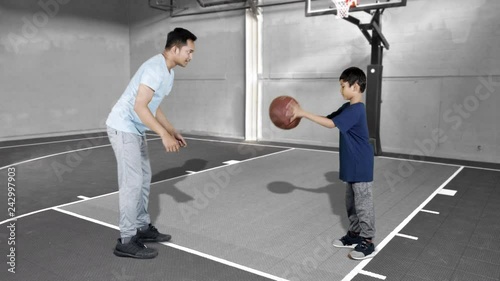 JAKARTA, Indonesia - January 08, 2019: Young man teaching his son to play basketball at indoors basketball court. Shot in 4k resolution photo