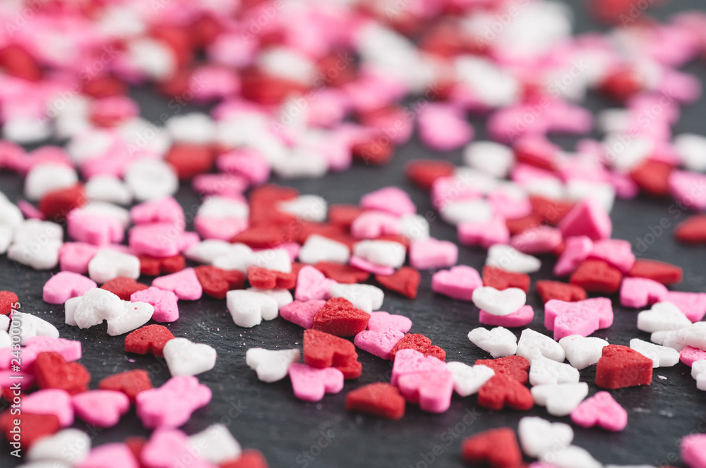 abstract closeup of little pink red and white heart sprinkles on a black slate background abstract closeup of little pink red and white heart sprinkles on a black slate background